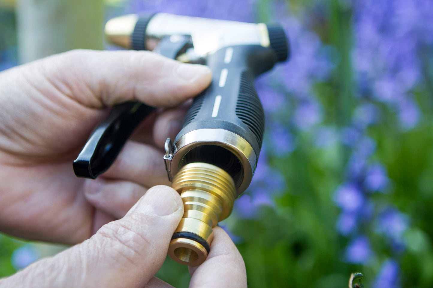 Person holding a garden hose nozzle with a blurred natural background