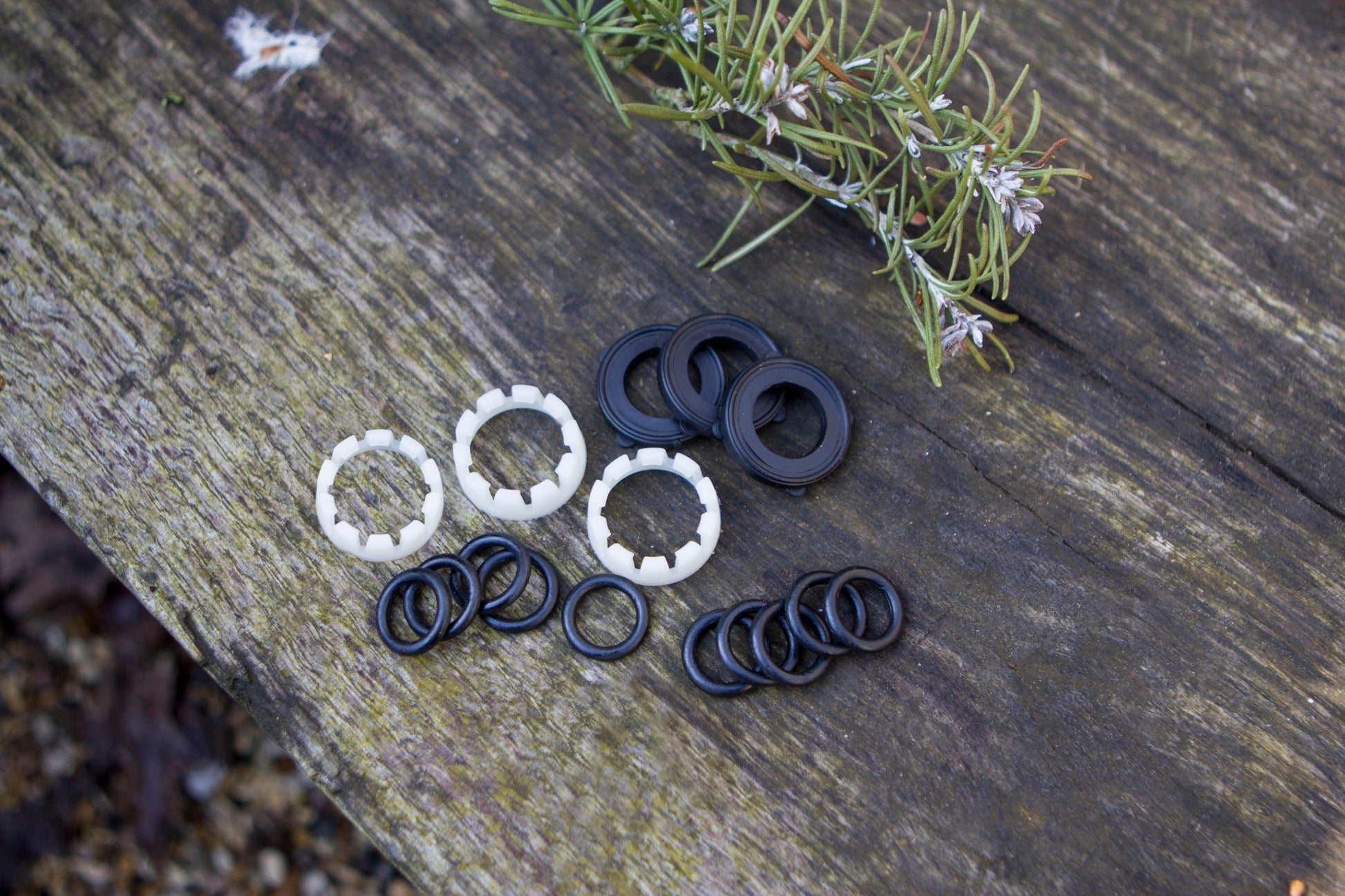Black and white rubber washers on a wooden surface with rosemary sprigs.