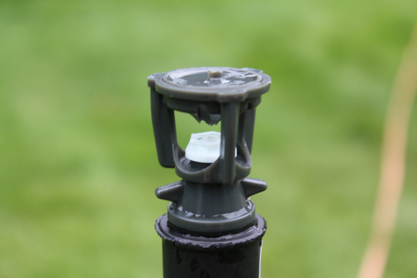 Close-up of a black garden sprinkler head with a blurred green lawn background