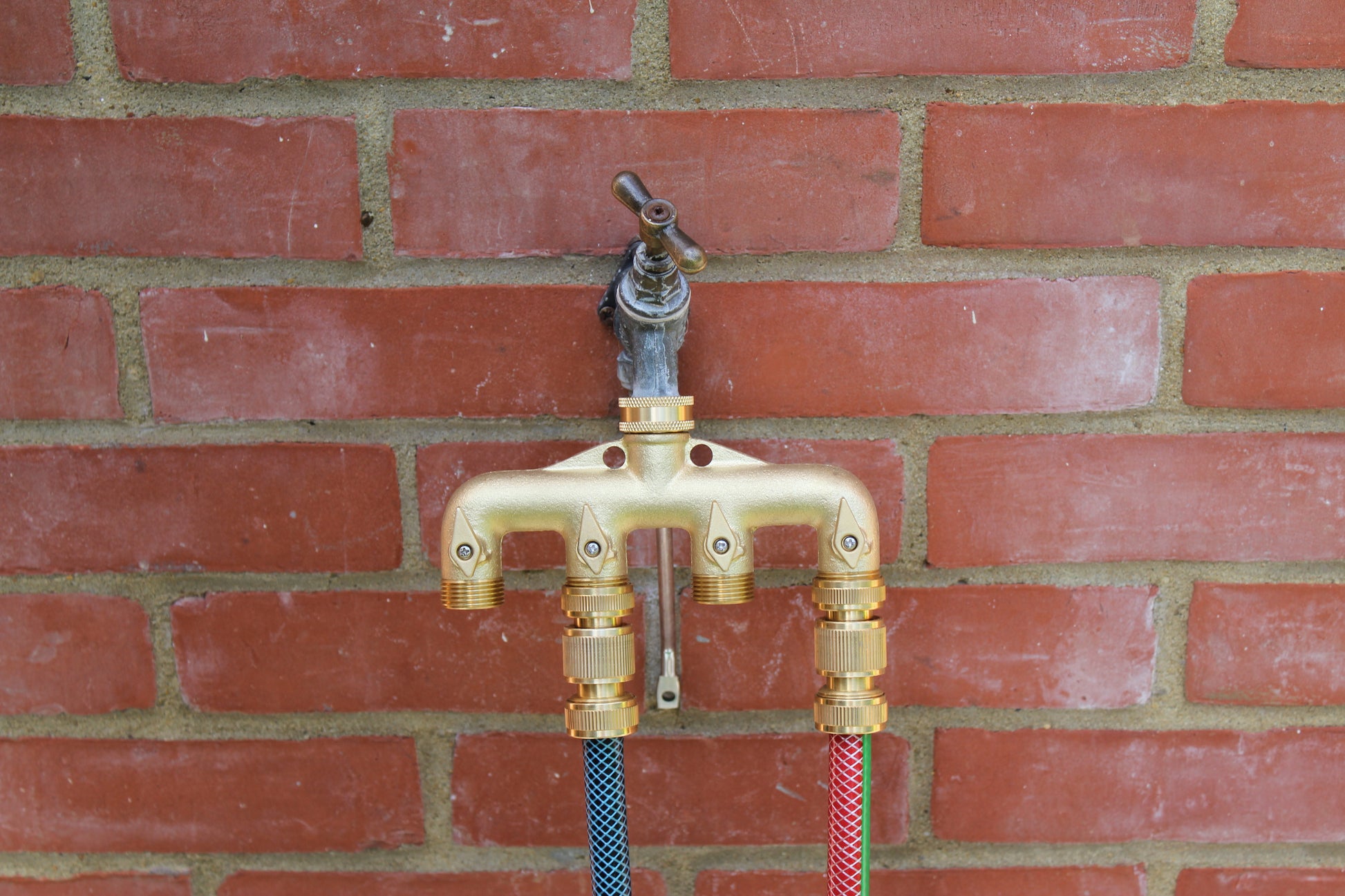 Brass outdoor faucet with hoses attached to a brick wall