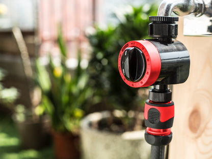 Black and red garden valve attached to a pipe with a blurred outdoor background