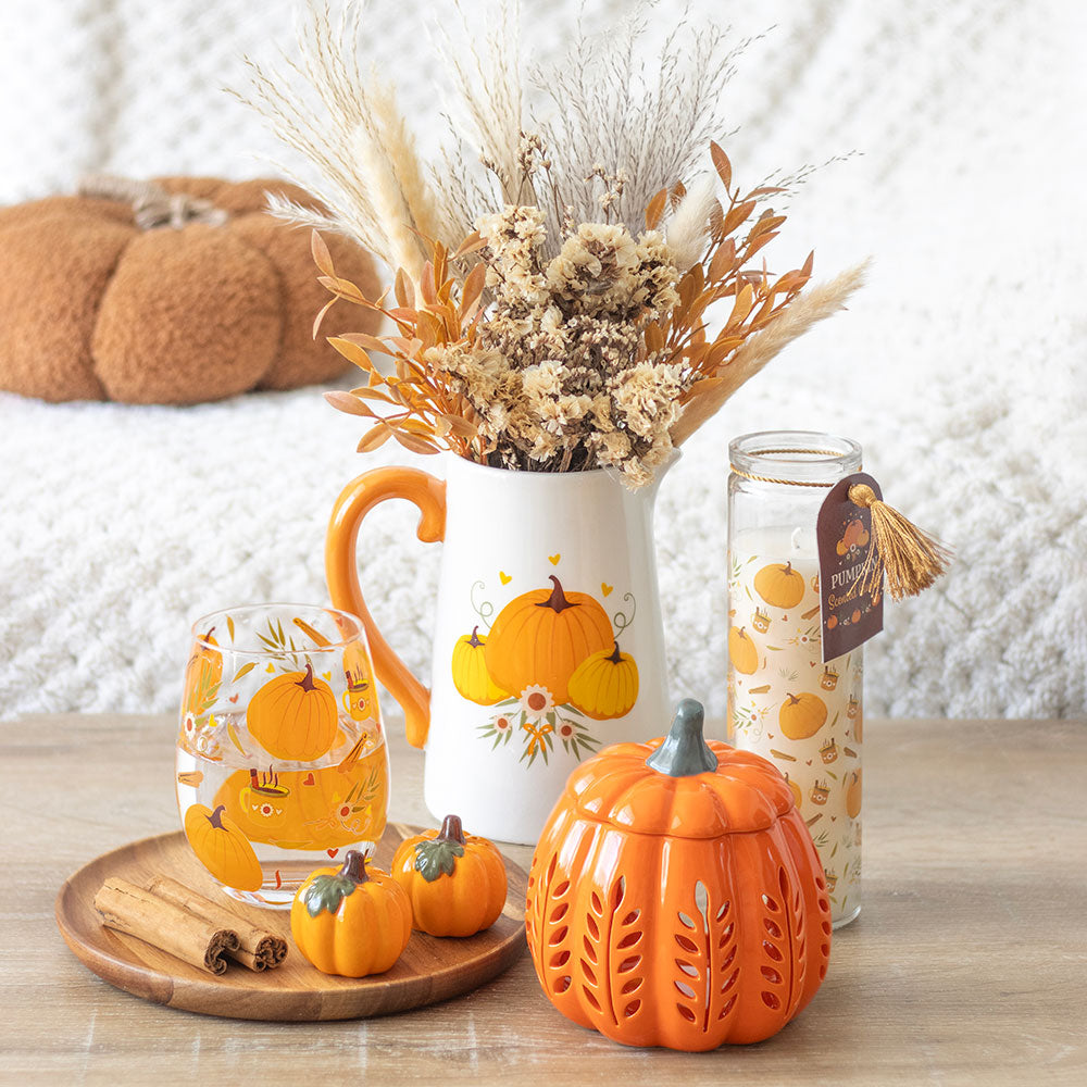 Autumn-themed decor items including a pitcher, mug, and pumpkin-shaped container on a wooden surface.