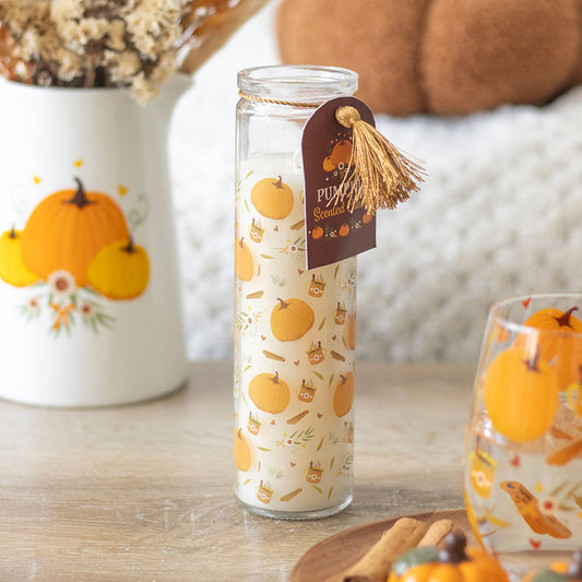 Glass bottle with pumpkin pattern and tag on a wooden surface with decorative items.