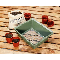 Green seedling tray with small pots and soil on a wooden surface
