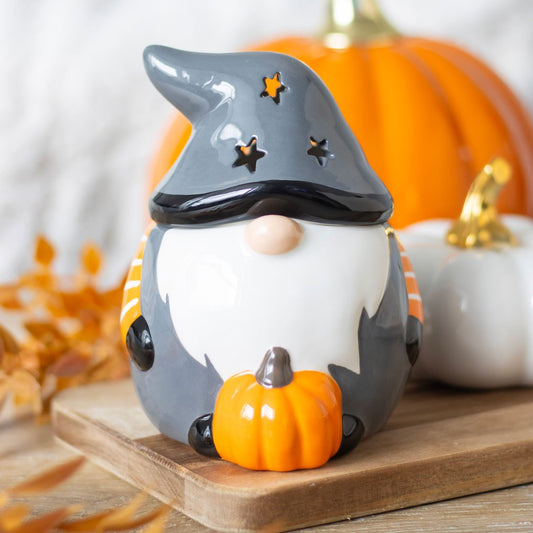 Decorative gnome figurine with a witch hat and pumpkin on a wooden surface with pumpkins in the background.
