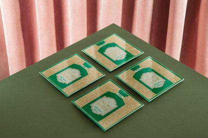 Four green and gold cards on a green surface with pink curtains in the background
