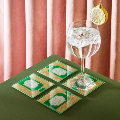 Set of four green and gold coasters with a glass of water on a green surface.