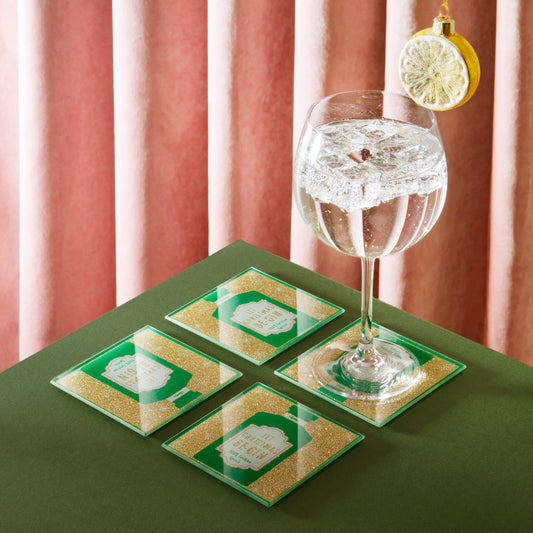 Set of four green and gold coasters with a glass of water on a green surface.