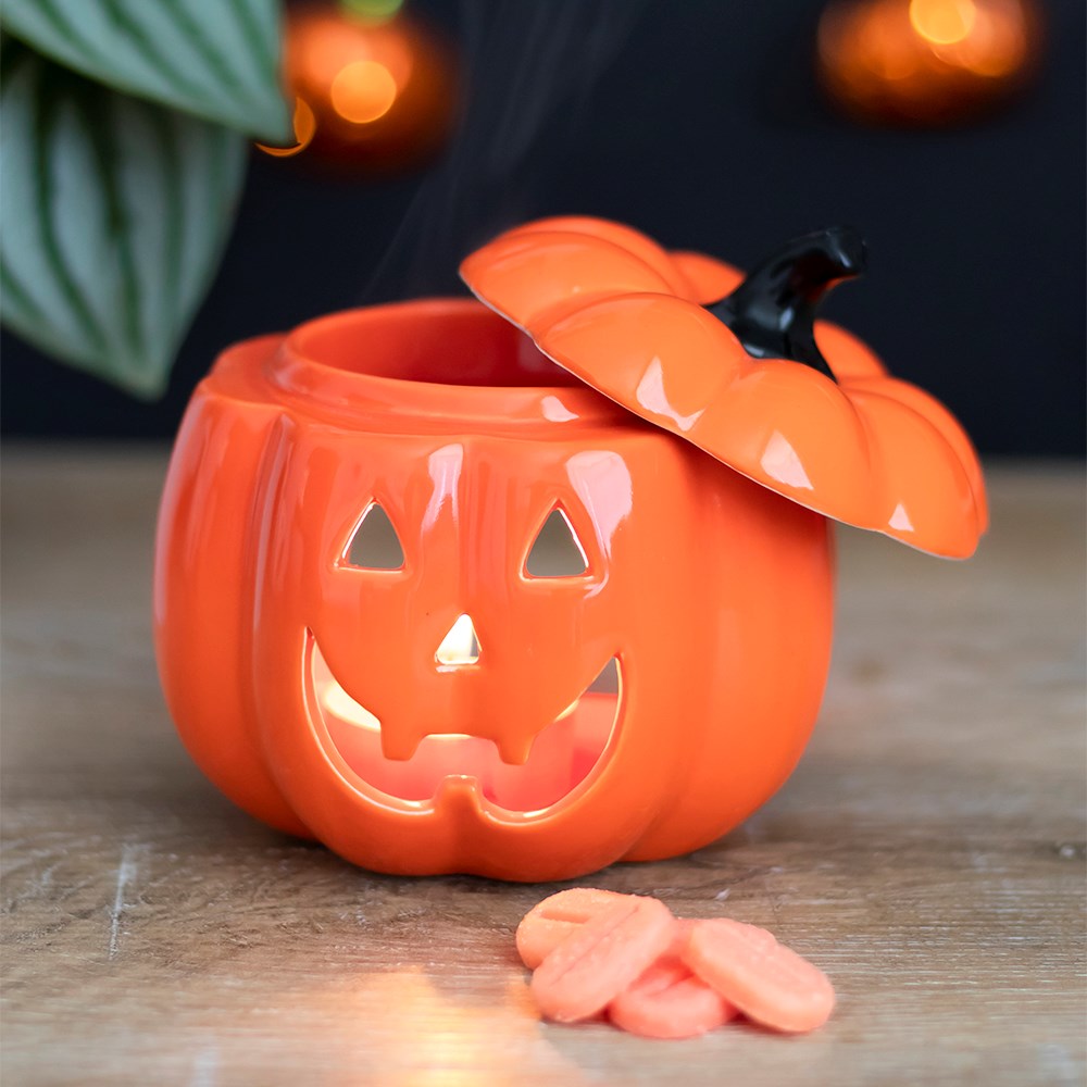 Orange ceramic pumpkin with a lid on a wooden surface, featuring a carved face.