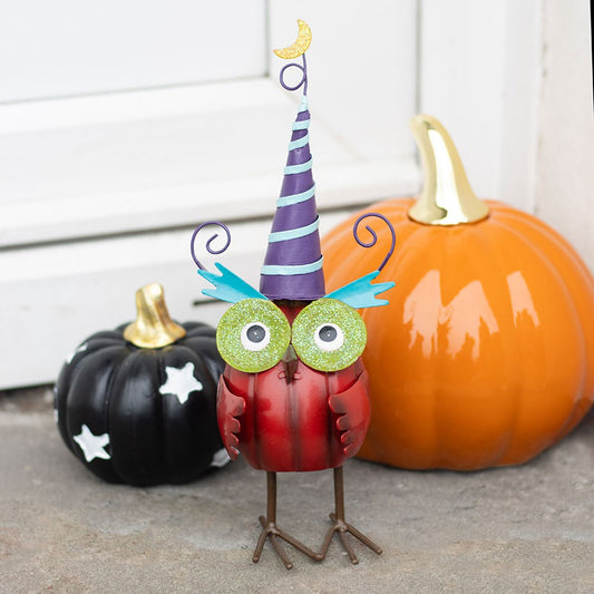 Decorative owl with a witch hat in front of pumpkins on a neutral background