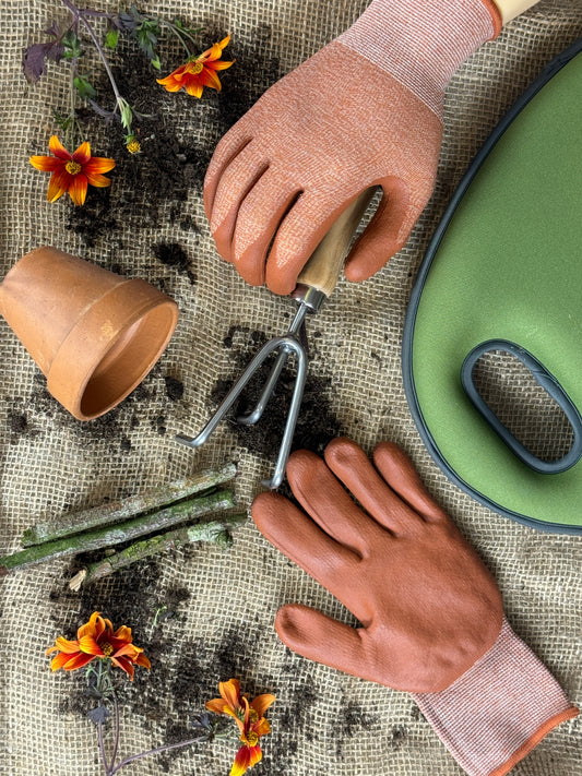 Gardening tools and gloves on a textured surface with flowers.