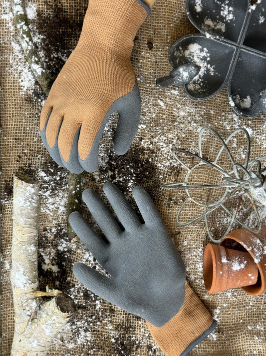 Pair of gardening gloves on a rustic surface with gardening tools.