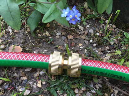 Red and green garden hose with brass fitting on a garden bed with flowers and rocks.