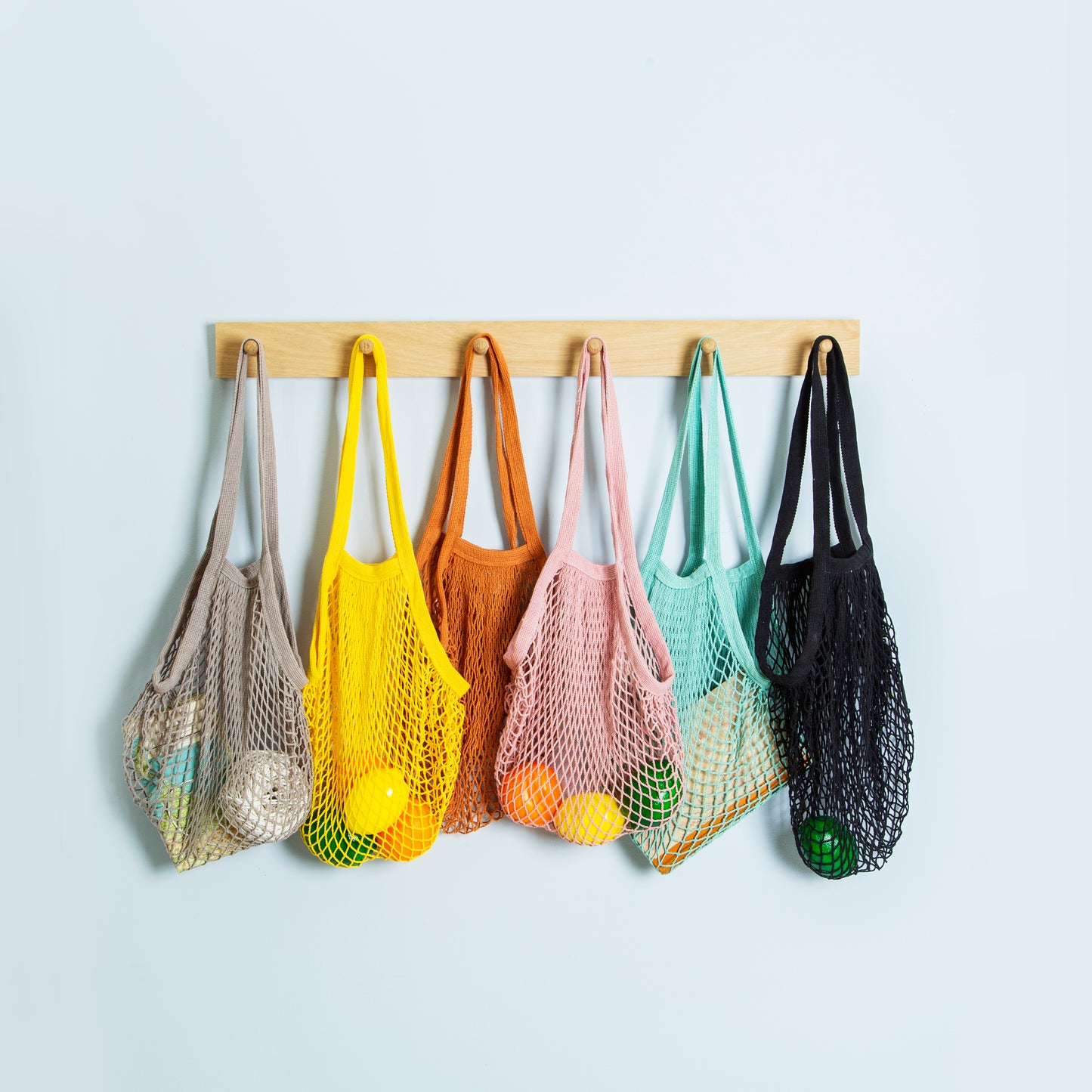 Different coloured string shopping bags hanging on wall hooks