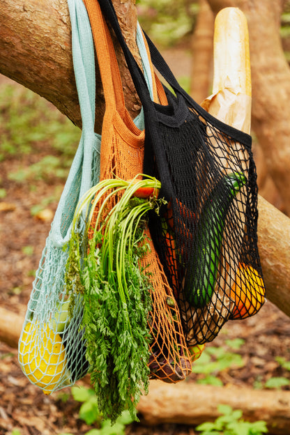 Black string shopping bag filled with bread and carrots in an outside setting