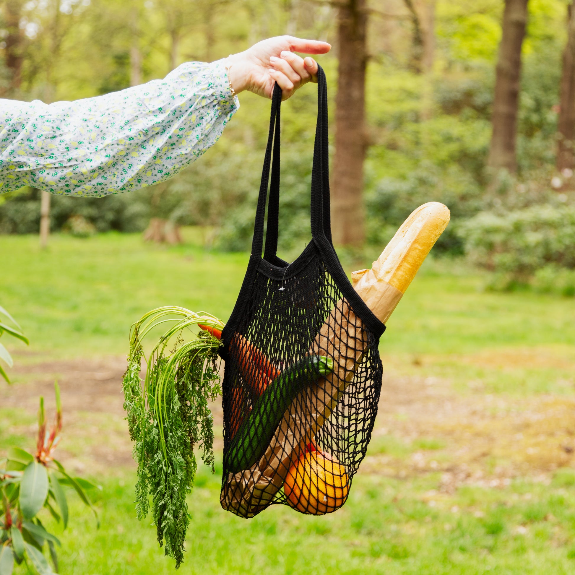 Black string shopping bag filled with bread and carrots in an outside setting