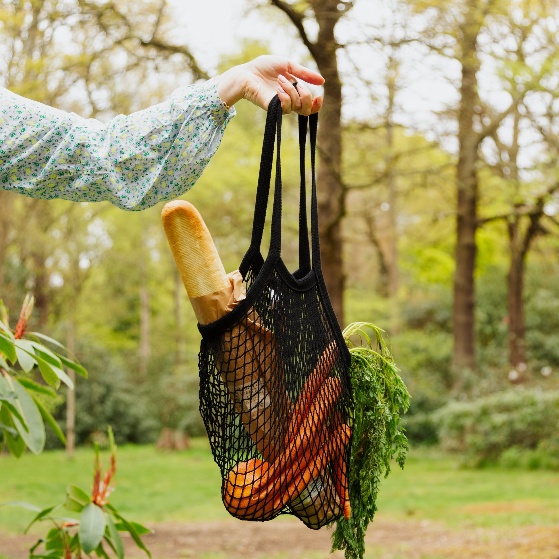 Black string shopping bag filled with bread and carrots in an outside setting