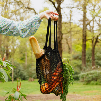 Black string shopping bag filled with bread and carrots in an outside setting