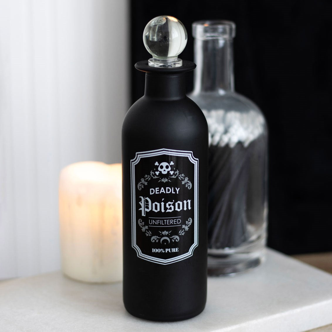 Black bottle labeled 'Deadly Poison' with a skull and crossbones design, next to a lit candle.