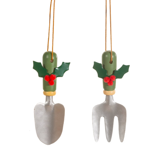 Two gardening tool-shaped Christmas ornaments with holly leaves and berries on a white background.