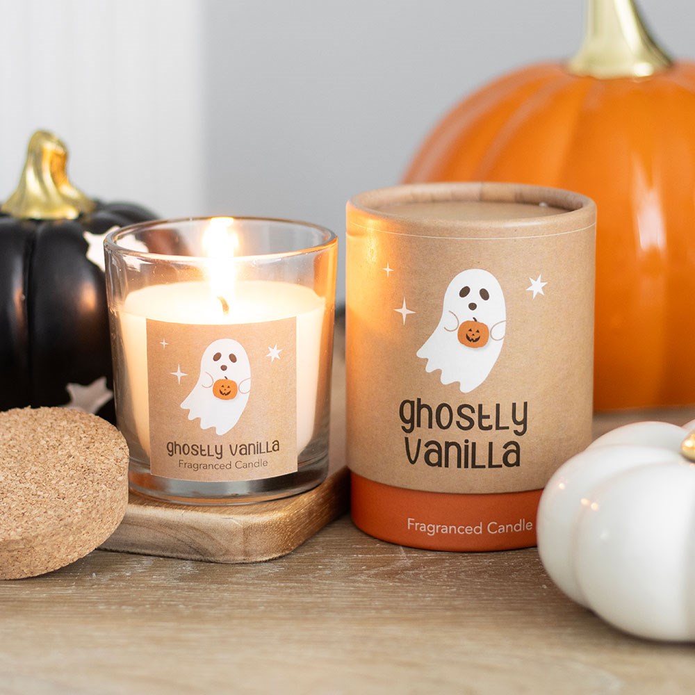 Ghostly Vanilla scented candle with packaging surrounded by pumpkins and decorative items on a wooden surface.