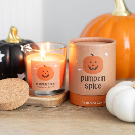 Pumpkin spice candle with packaging and pumpkins on a wooden surface