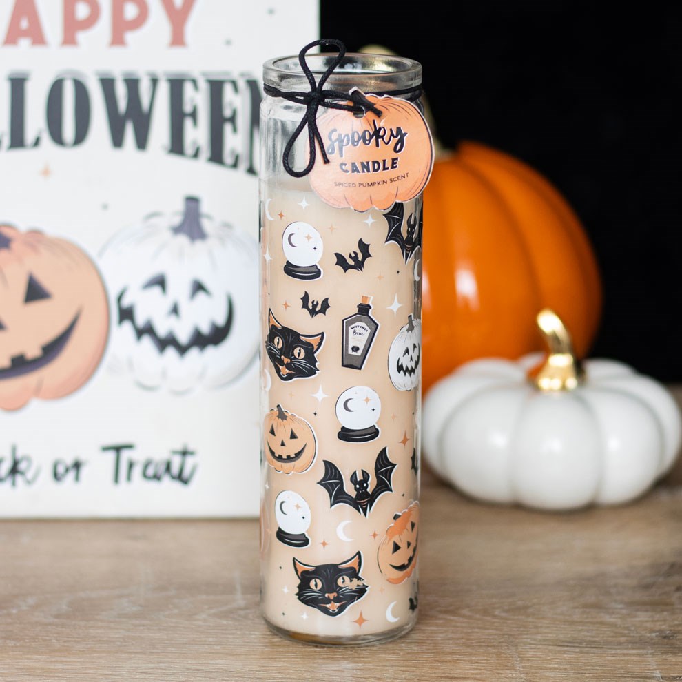 Halloween-themed candle with decorative design on a wooden surface with pumpkins and a 'Happy Halloween' sign.