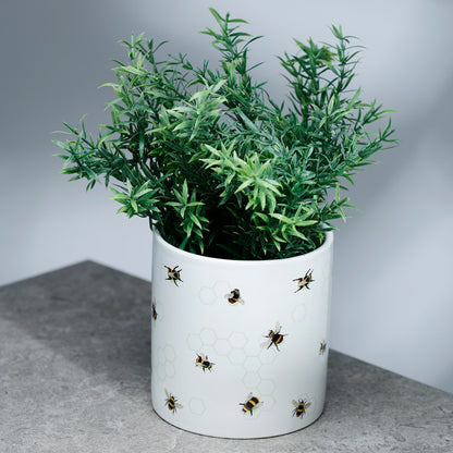 White pot with green plant and bee pattern on a gray surface