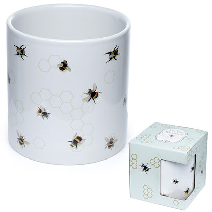 White mug with bee and honeycomb pattern next to a matching candle in a box on a white background