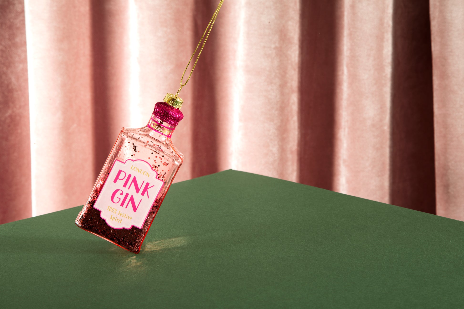Pink Gin bottle ornament on a green surface with a striped background