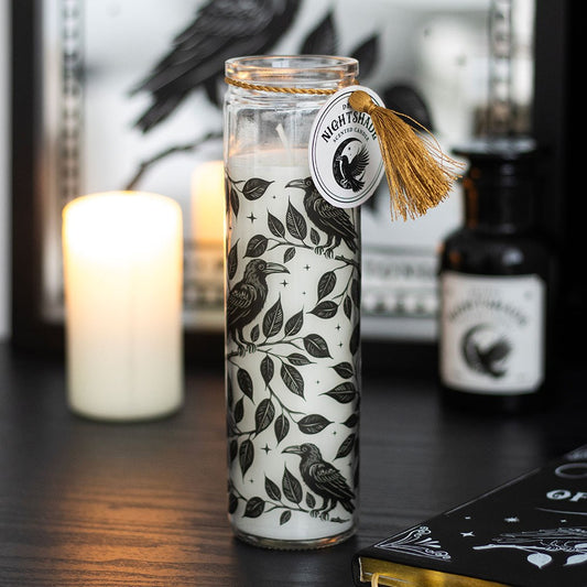 Decorative candle with bird and leaf pattern in a glass jar on a dark surface.