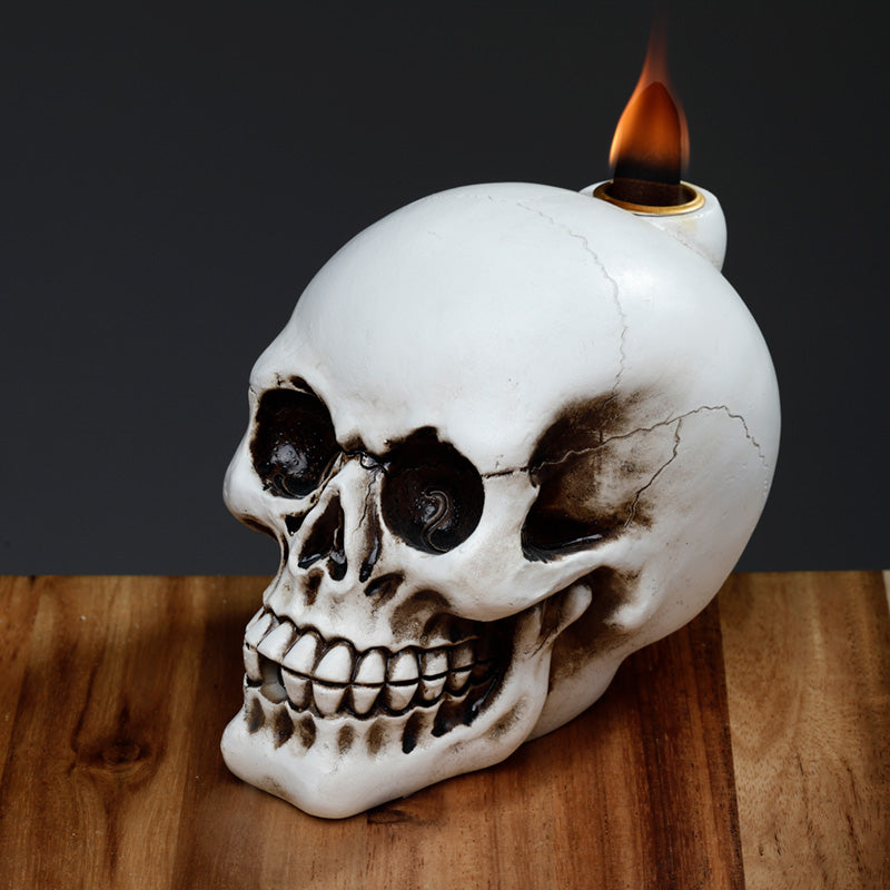 Skull-shaped candle holder with a lit candle on a wooden surface