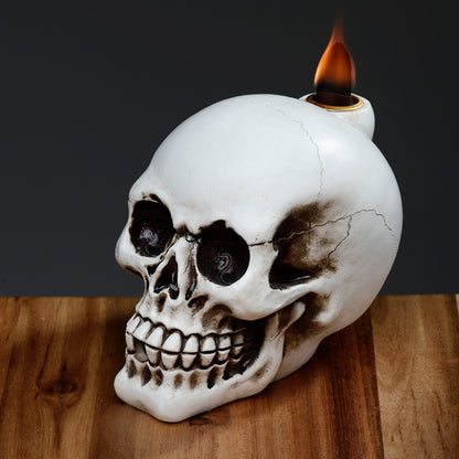 Skull-shaped candle holder with a lit candle on a wooden surface