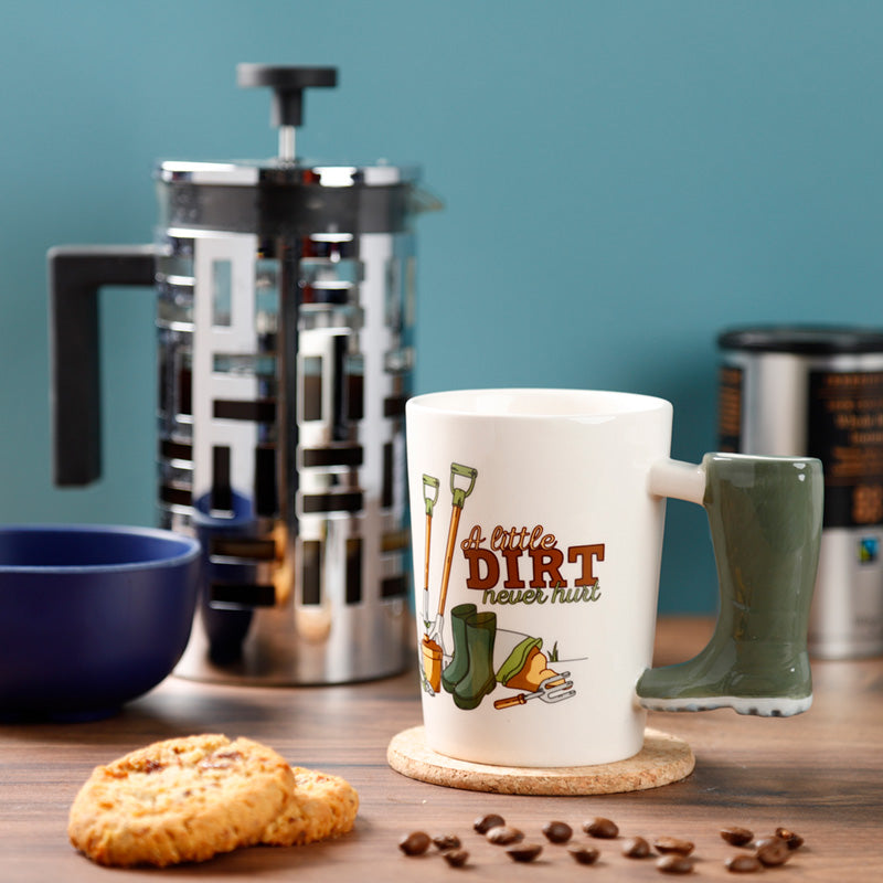 White mug with gardening-themed design on a wooden surface with coffee-making equipment and cookies.
