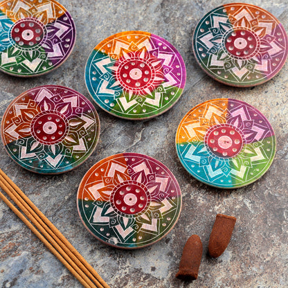 Colorful mandala-patterned incense cones on a stone surface with incense sticks.