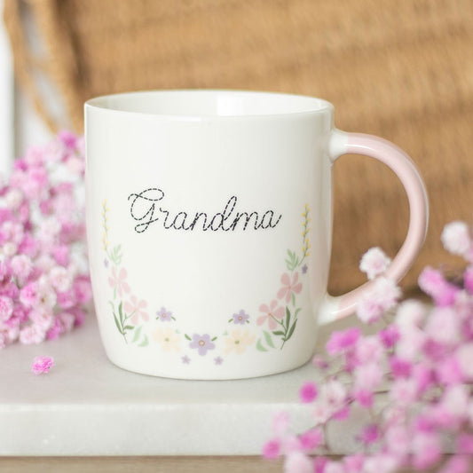 White mug with 'Grandma' and floral designs on a wooden surface with pink flowers.