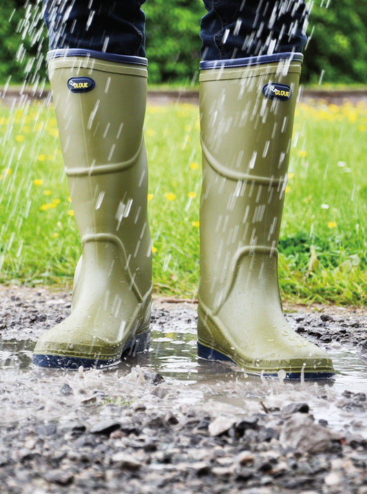 Green wellington boots being worn in a rain-soaked outdoor setting with grass and water.