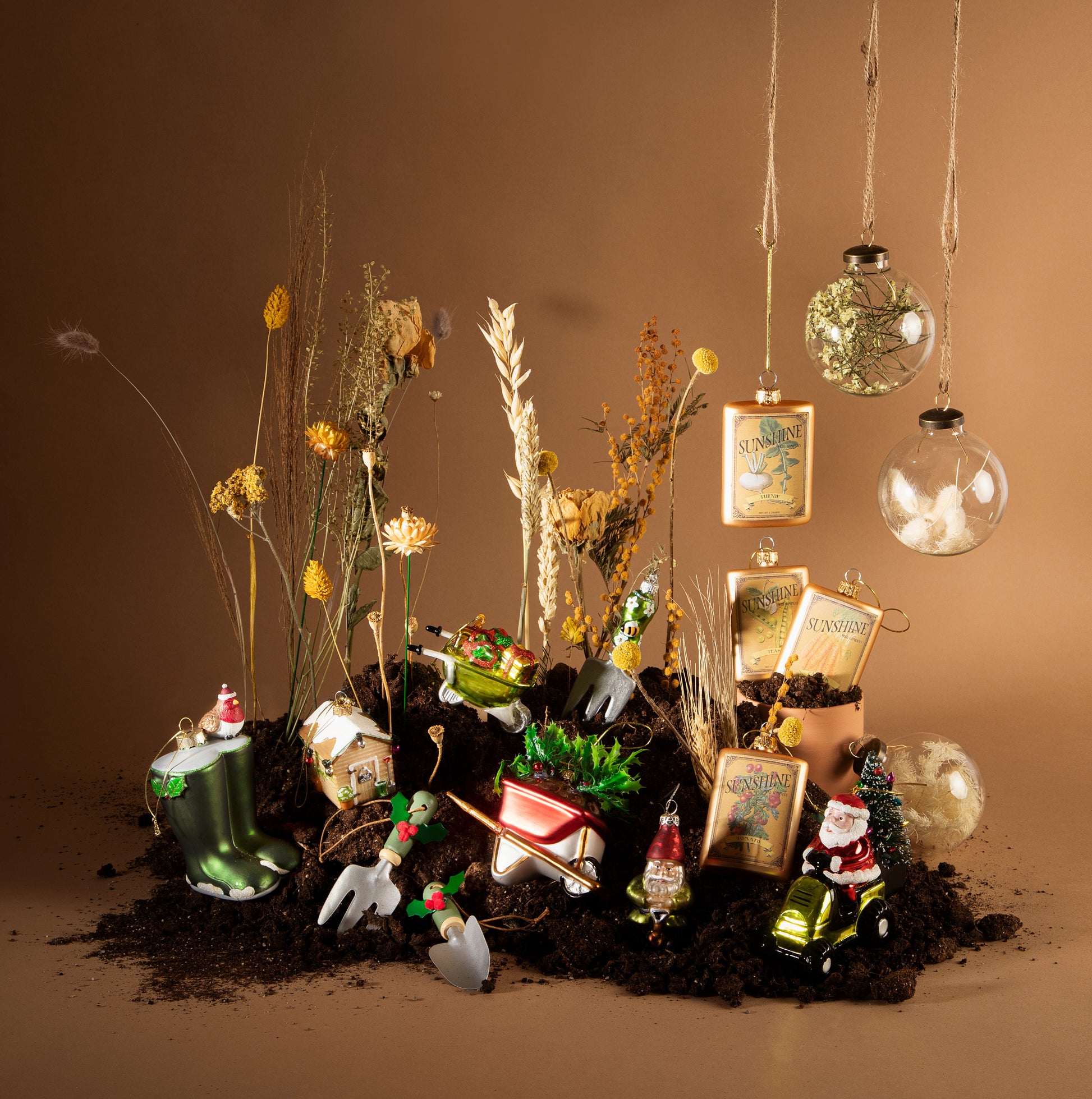 Decorative arrangement with small gardening-themed figurines, plants, and ornaments on a brown background.