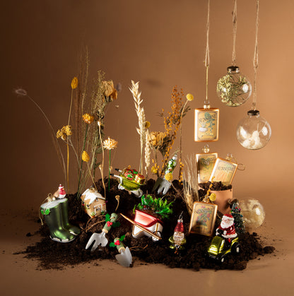 Decorative arrangement with small gardening-themed figurines, plants, and ornaments on a brown background.