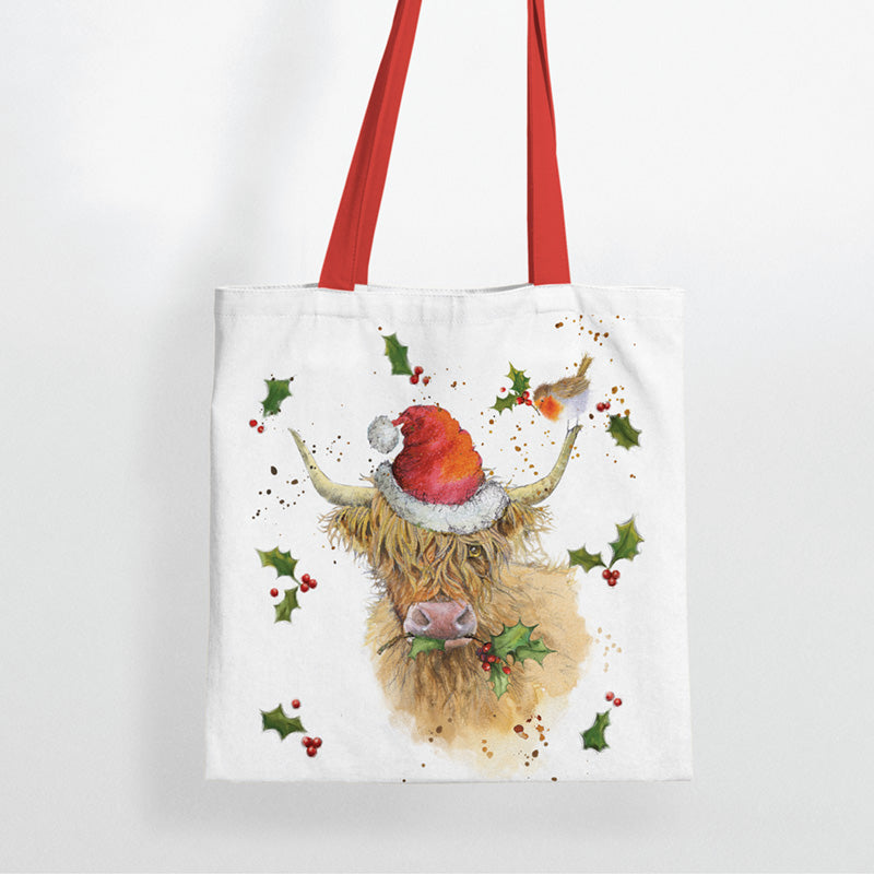 Tote bag with a highland cow wearing a Santa hat and holly leaves on a white background