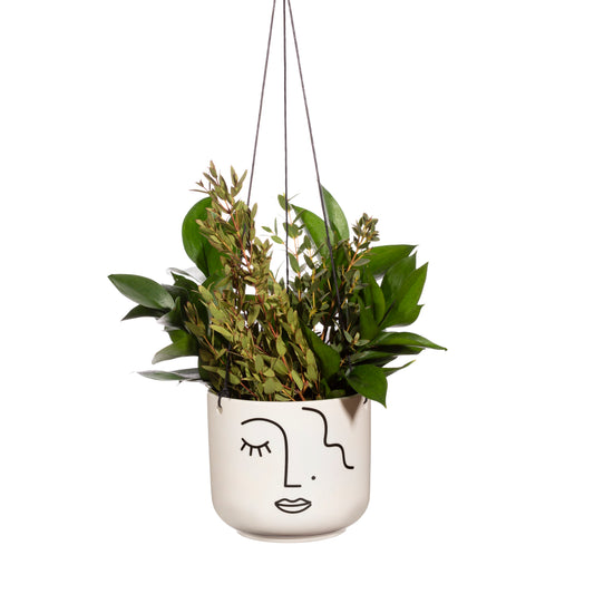 Hanging planter with green leaves in a white pot featuring a face design on a white background