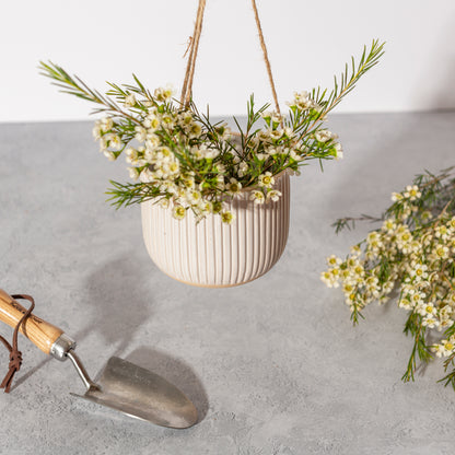 White hanging planter with greenery on a gray surface with a trowel.