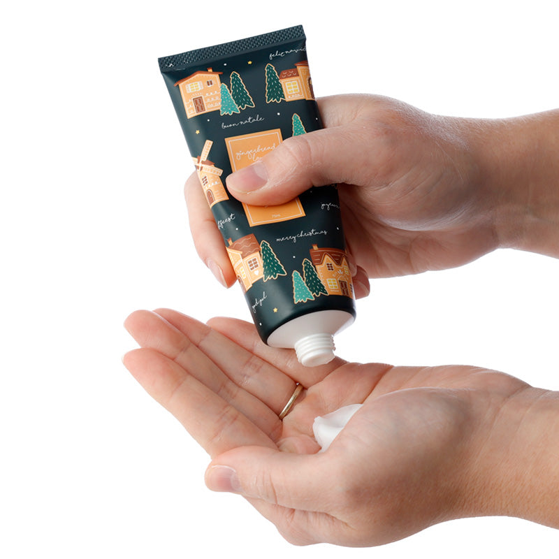 Hand holding a tube of hand cream with a decorative label, applying cream to the palm.