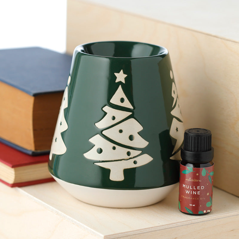 Green ceramic diffuser with Christmas tree design and a bottle of mulled wine fragrance oil on a wooden surface.