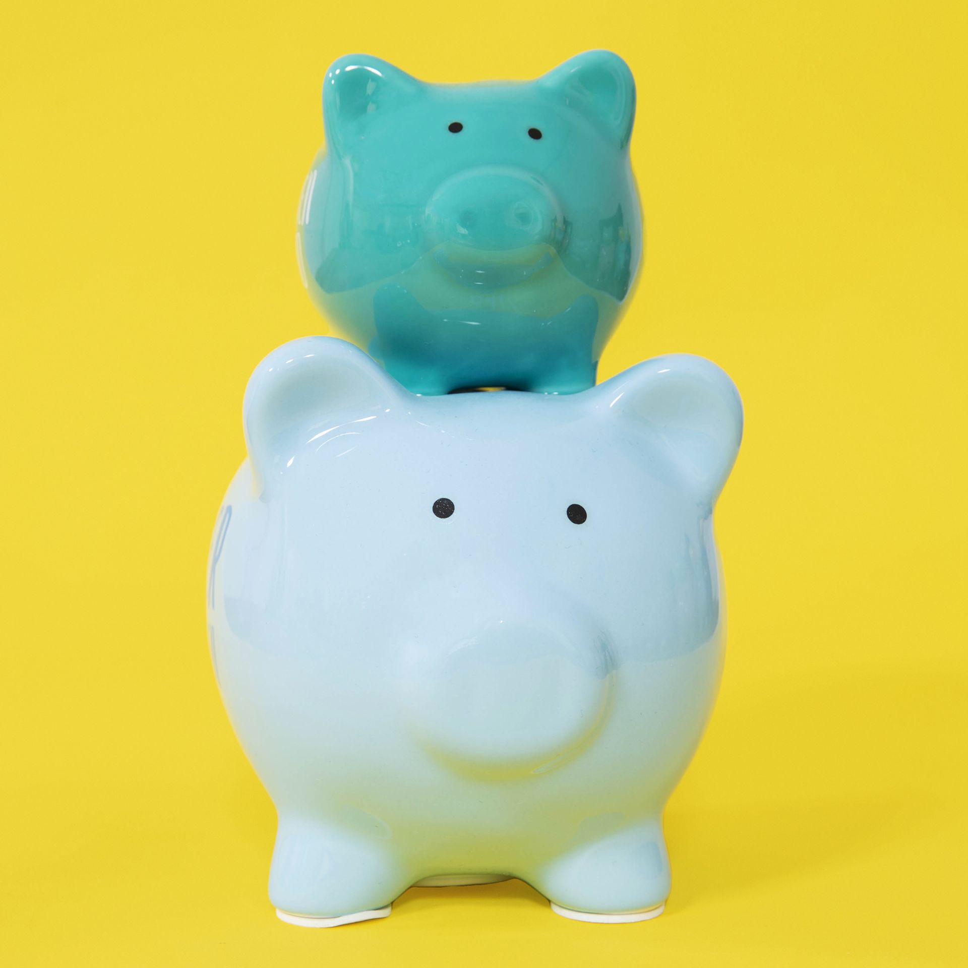 Two piggy banks, one blue and one green, stacked on a yellow background.