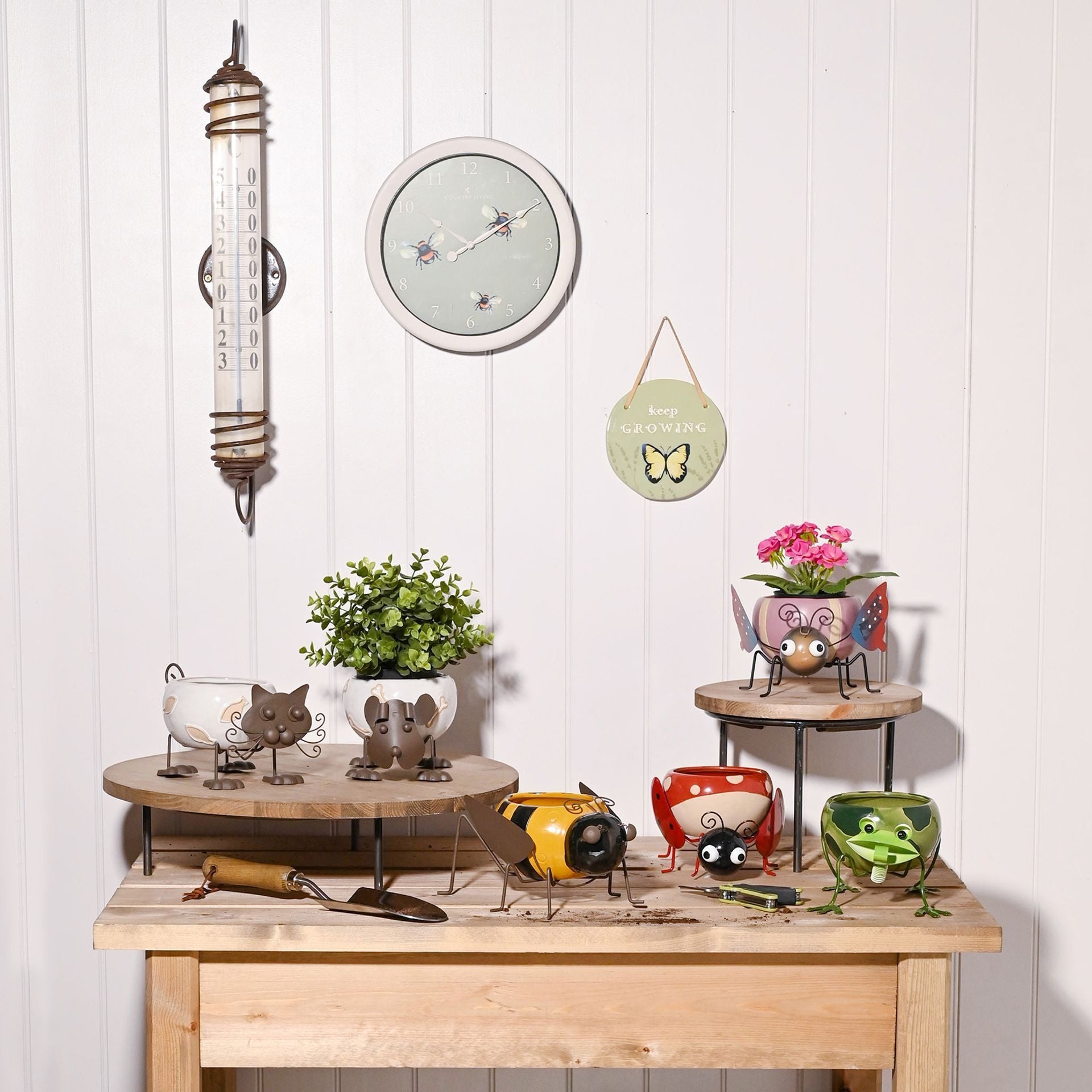 Decorative items including a thermometer, clock, and small plants on a wooden surface with a white paneled wall background.