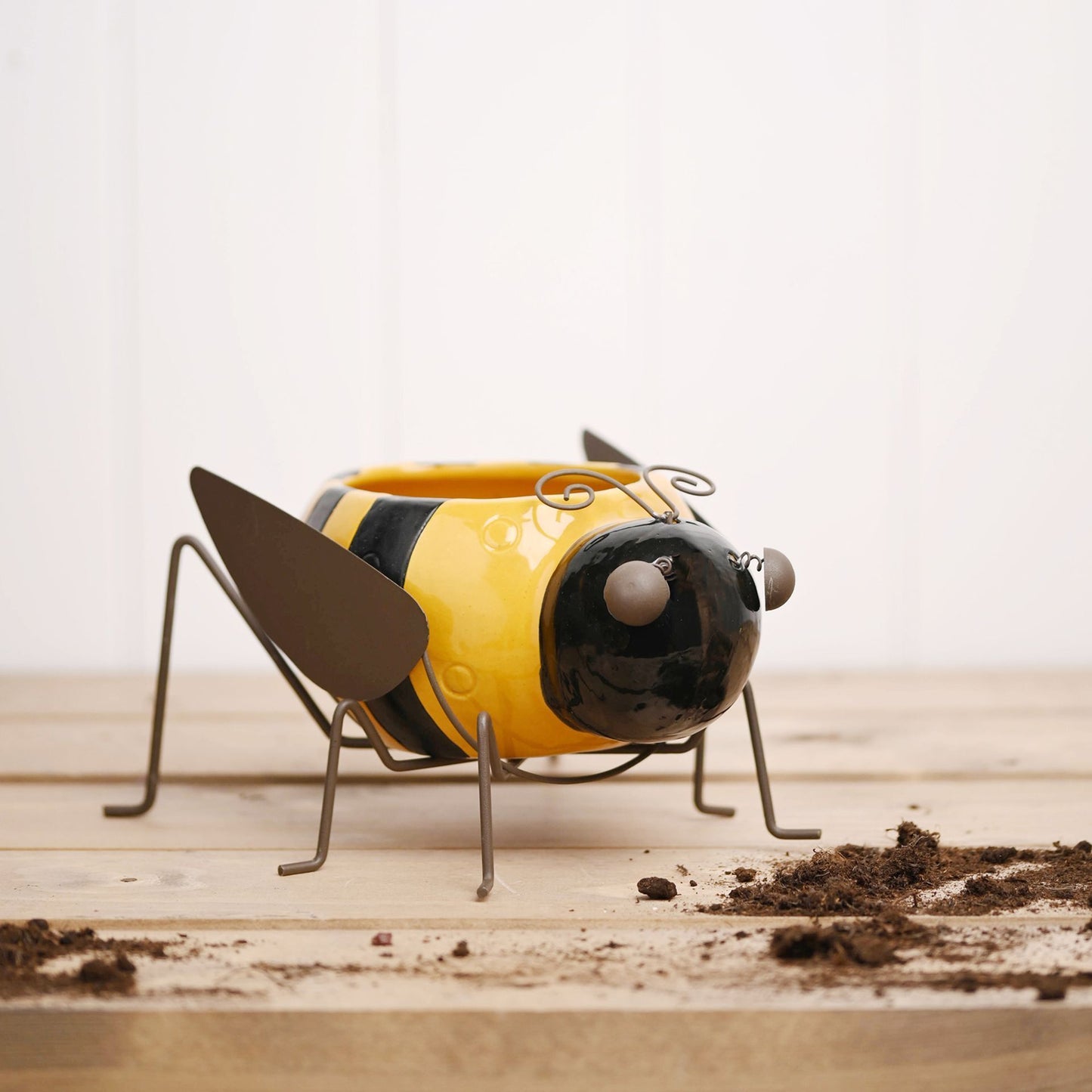 Yellow and black bee-shaped planter on a wooden surface with soil