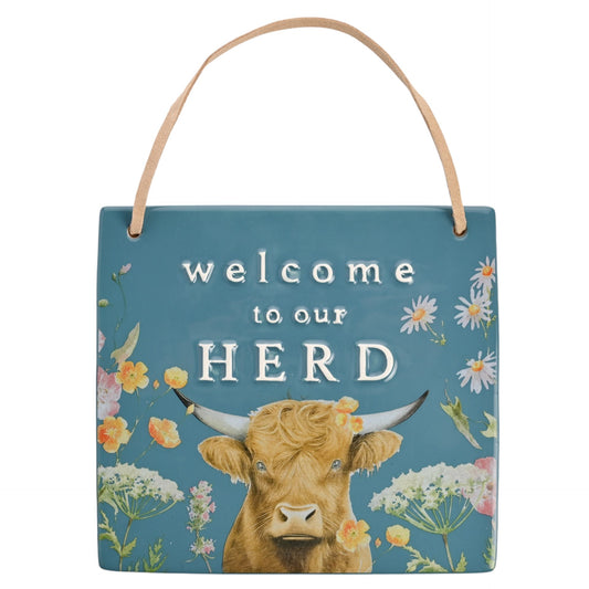 Decorative sign with a cow illustration and 'welcome to our HERD' text on a blue background.