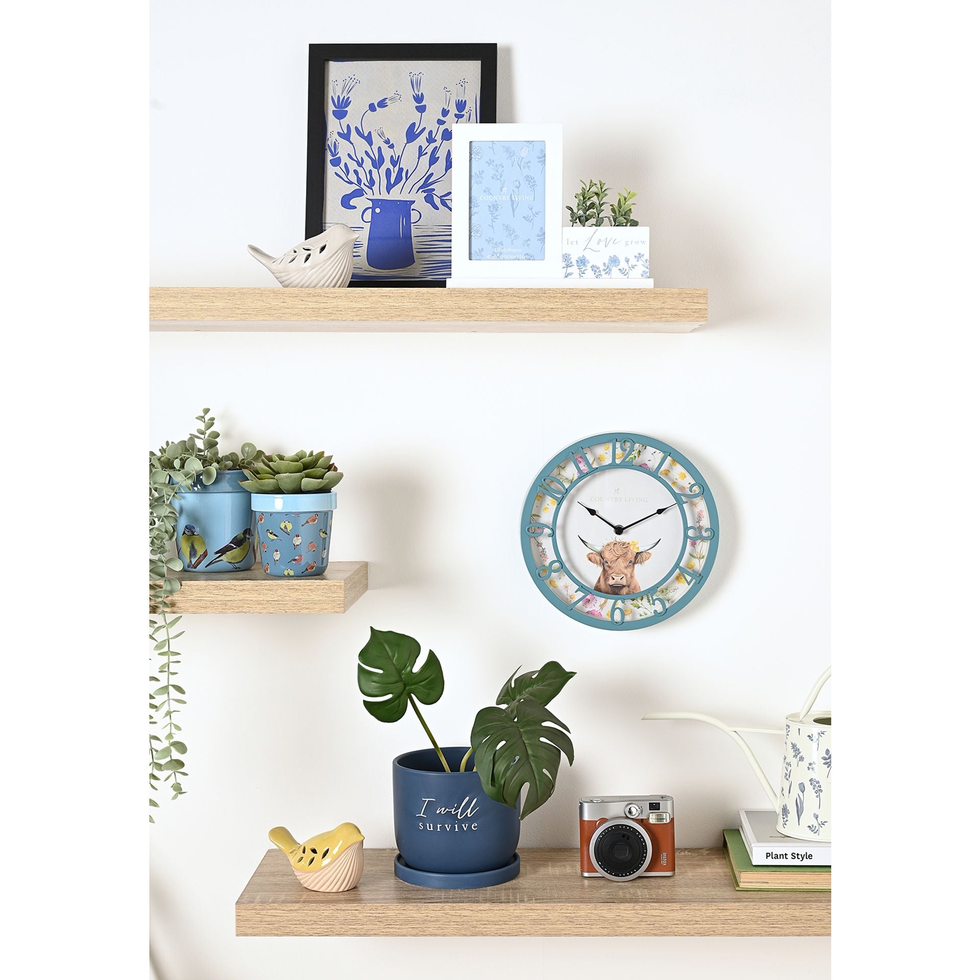Decorative wall clock with cow design on a shelf with plants and decor items.
