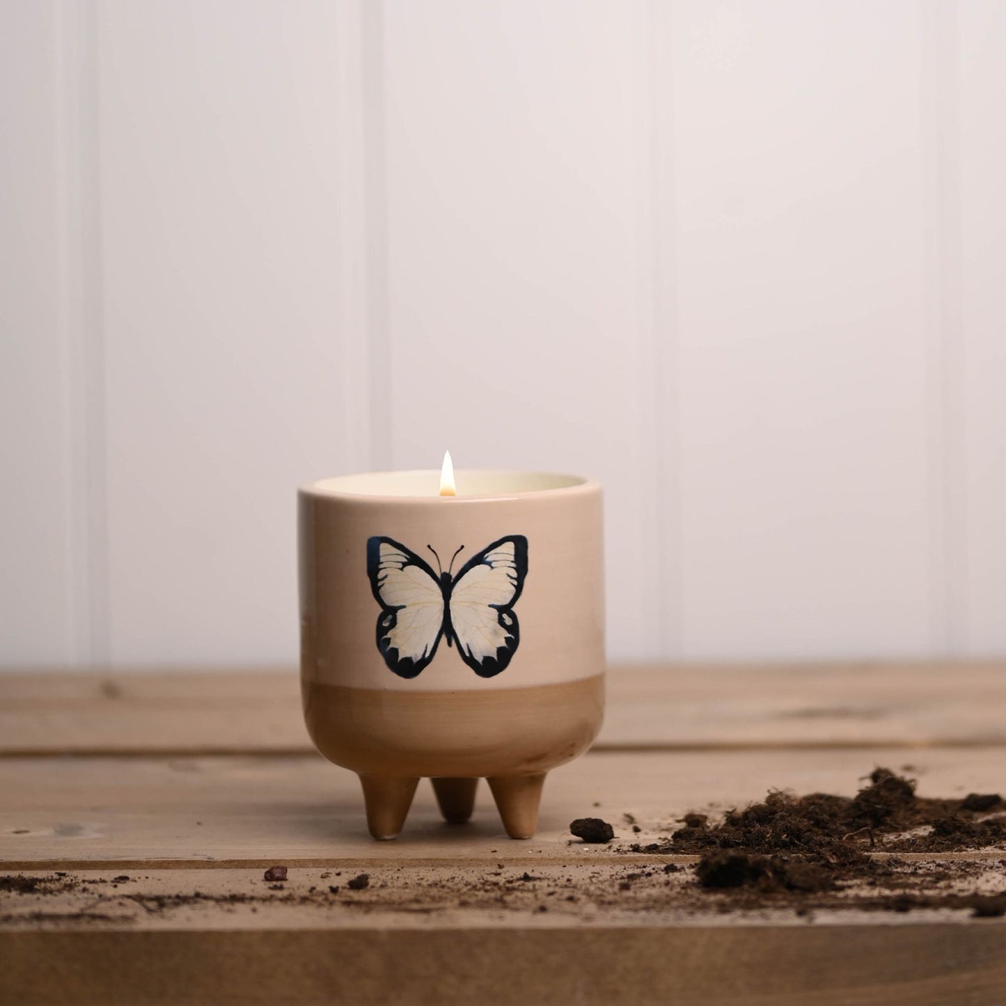 Candle in a pot with a butterfly design on a wooden surface